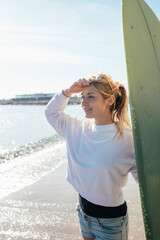 Caucasian girl looking at the ocean with surfboard