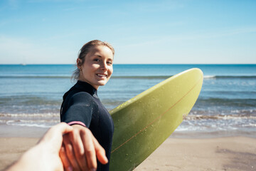 Portrait of young girl holding hand of her boyfriend leading him walking on the beach to surfing. Summer and vacation concept.