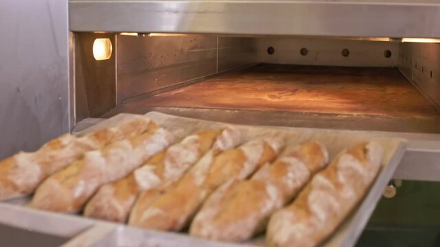 The baker pulls the hot baguettes out of the oven.