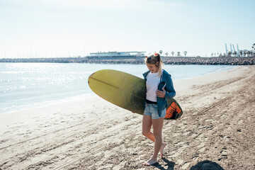 Young girl walking along the shore with surfboard. Vacation concept.