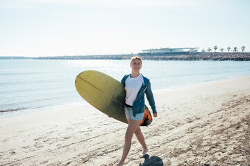 Happy girl walking along the shore carrying a surfboard