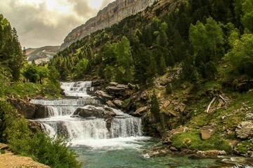 Fototapeta na wymiar Cascada de Soaso (también conocida como Escalones de Soaso) en el río Arazas, Pirineos, Huesca, España. Un hermoso paisaje natural del bosque de pinos en las laderas de la montaña en verano.
