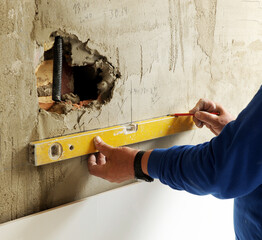 A bricklayer marking a horizontal line with the level tool on the wall during the complete...