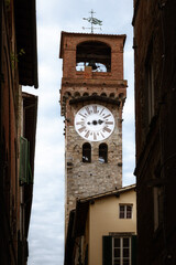 Famous Torre delle Ore (tower of the hours), ancient medieval turret clock in the town center of Lucca (Tuscany, Italy), landmark and symbol of the city seen from the nearby narrow alleys - obrazy, fototapety, plakaty
