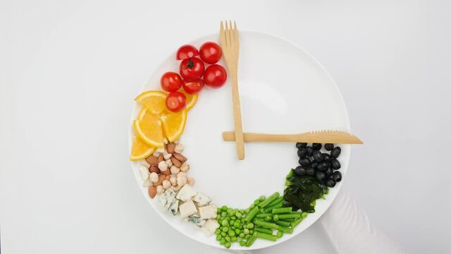 Colorful food and cutlery arranged in the form of a clock on a plate. Intermittent fasting, diet, weight loss, lunch time concept.