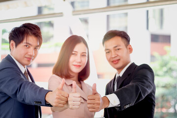 Group of three Asian businessman and woman confidential standing and giving thumbs up to camera, businesswoman holding digital tablet, businesspeople in downtown city.