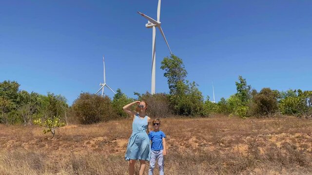 Slowmotion shot. Young woman and her son visit a wind turbine farm in a semidesert environment. Wind energetics concept