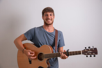 Obraz premium Portrait of a young musician who plays the guitar and smiles. Studio photo of an Artist isolated on white background. Young smiling man