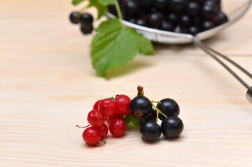 a bunch of black and red currants on a wooden background and berries in a colander