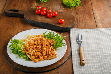 A plate of bolognese pasta decorated with herbs on a wooden table next to a gray napkin and a fork.