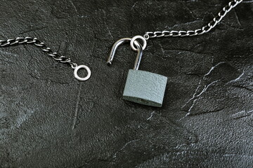 Fototapeta na wymiar unlocked padlock with chain on black concrete background with copy space