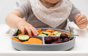 Unrecogniable caucasian baby about 1 year old, eating from silicone plate of fresh vegetables, fruits, berries. Self-feeding for kids. Baby-led weaning idea. Healthy nutrition of solid food for infant