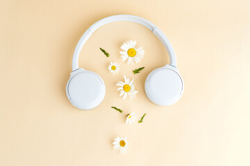Music or podcast background with headphones and daisy (camomile) flowers on yellow background. Summer podcast. Top view, flat lay