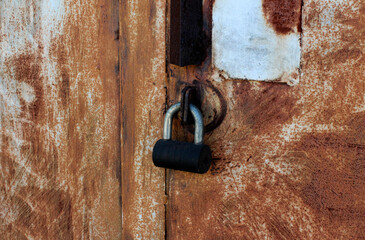 Rusty metal door closed with black metal lock