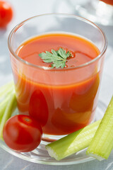 A glass with fresh tomato juice, celery, parsley and ripe tomatoes on a light wood background