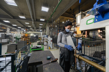 Fototapeta premium woman working in the metal industry in the production of new machines wears a face mask during work due to the coronavirus pandemic