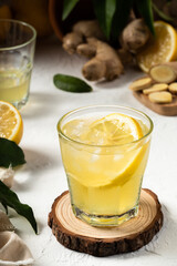 Detox and fresh lemon drink with ginger and a slice of lemon inside the glass, as an immune boosting and weight loss drink, on a white textured surface, soft light