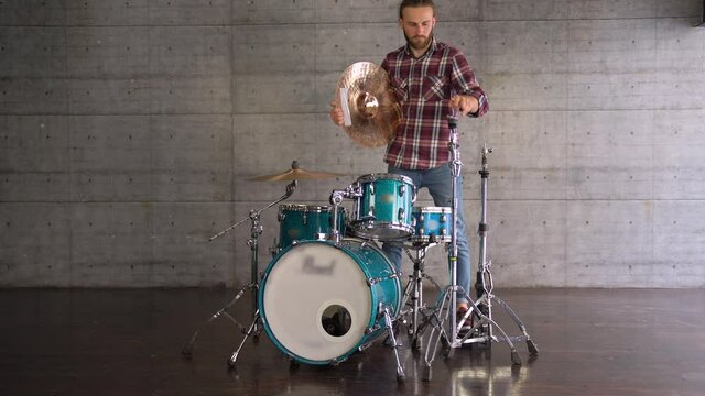 WIDE Shot Young bearded brutal Man Mounting Hi-Hat Cymbals On A Stand-Setting Up A Drum-set Before Rehearsing.