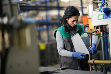 a woman working in a modern metal factory assembles parts for a new machine