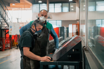 two workers wearing a face mask due to a coronavirus pandemic are programming a modern cnc machine