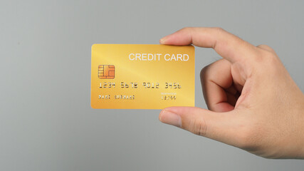 Hand is holding gold color credit card isolated on grey background.