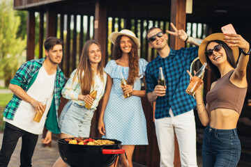 young friends making barbecue and drinking drinks, preparing meat in nature, having fun and taking selfie , youth lifestyle, summer concept