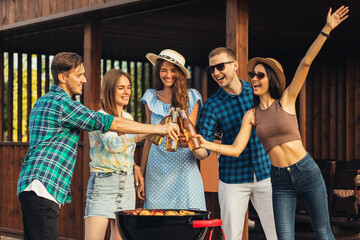 Group of young friends having fun at a party outdoors, drinking cold drinks, making barbecue and grilled vegetables