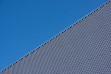 blue sky and gray covered building wall with decorative metal sheet on a sunny day.