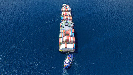Aerial drone photo of tow - tug boat assisting by pulling or pushing container ship to anchor in...