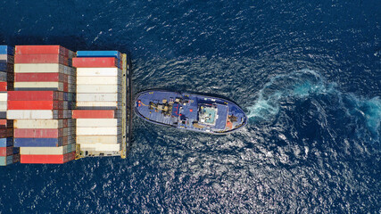 Aerial drone photo of tow - tug boat assisting by pulling or pushing container ship to anchor in terminal port
