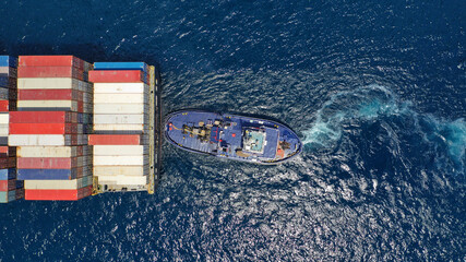 Aerial drone photo of tow - tug boat assisting by pulling or pushing container ship to anchor in...