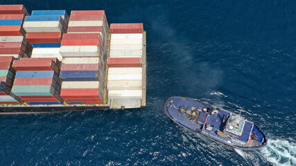 Aerial drone photo of tow - tug boat assisting by pulling or pushing container ship to anchor in...
