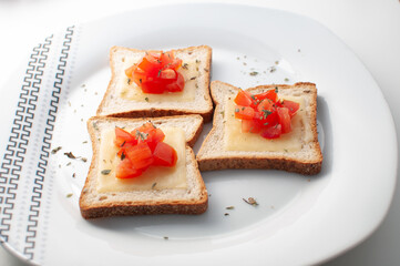 Top view of Toasts with melted cheease, chopped tomato and some oregano on a white plate on a white table or background.