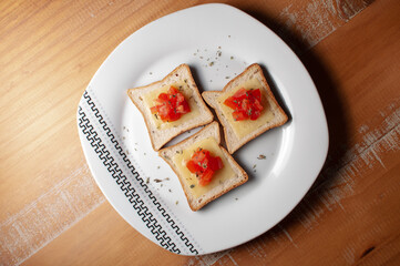 Top view of Toasts with melted cheease, chopped tomato and some oregano on a white plate on a wooden table or background. Top view.