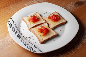 Top view of Toasts with melted cheease, chopped tomato and some oregano on a white plate on a wooden table or background.