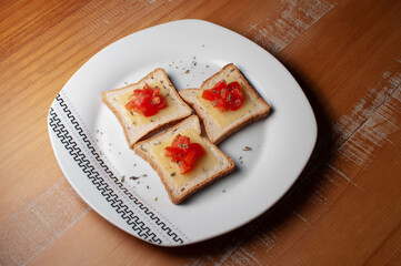 Top view of Toasts with melted cheease, chopped tomato and some oregano on a white plate on a wooden table or background.