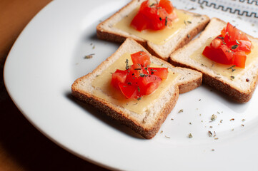 Top view of Toasts with melted cheease, chopped tomato and some oregano on a white plate on a wooden table or background.