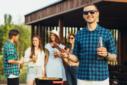 Young happy man in sunglasses having a group of friends having a barbecue with beer drinks having a rest in nature