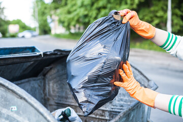 Cropped close up of a person putting garbage bag into trash can on city street