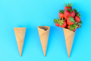 Three ice cream cones lie on a blue background and one waffle contains fresh strawberries, the other waffles are empty