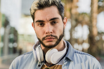 Young hispanic man having fun listening music with headphones with city on background - Focus on face