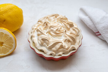 Lemon Merinque Tartlet with lemons and a dish towel in a red mini pie form