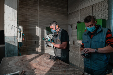 Industrial work during a pandemic. Two men work in a heavy metal factory, wearing a mask on their face due to a coronavirus pandemic