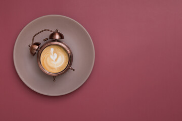 Alarm clock on a plate with frothy coffee and a pattern. Morning rise with coffee for breakfast concept. Copy space