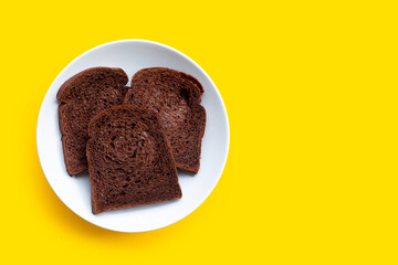 Dark cocoa bread in white plate on yellow background.