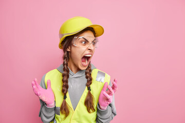 Irritated female contractor has two pigtails screams loudly expresses negative emotions wears...