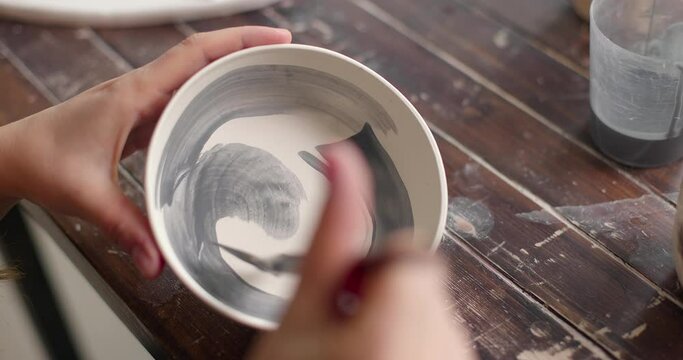 Pottery artist decorating ceramic pot at pottery workshop, slow motion