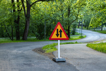 Yellow and red triangle two way traffic sign on a temporary stand with a curvy winding countryside...