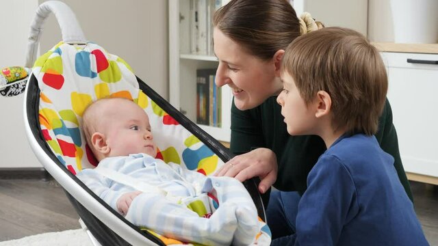 Happy baby boy rocking in chair next to his family sitting in living room. Child development and happy childhood