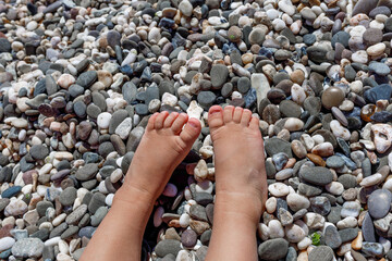 Baby small feet of a child close up on a background of stones on the beach on the sea in summer on vacation